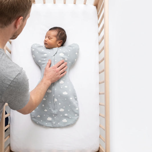 Newborn laid on their back on a bare firm crib surface in the LIOR Held Swaddle Sack.