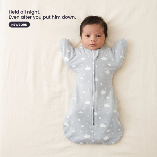 LIOR Held Swaddle Sack in Cloud Grey - newborn asleep on their back in a crib, wearing the zip-up sack.