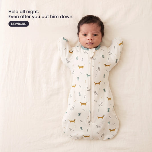LIOR Held Swaddle Sack in Cream Dachshund - newborn asleep on their back in a crib, wearing the zip-up sack.