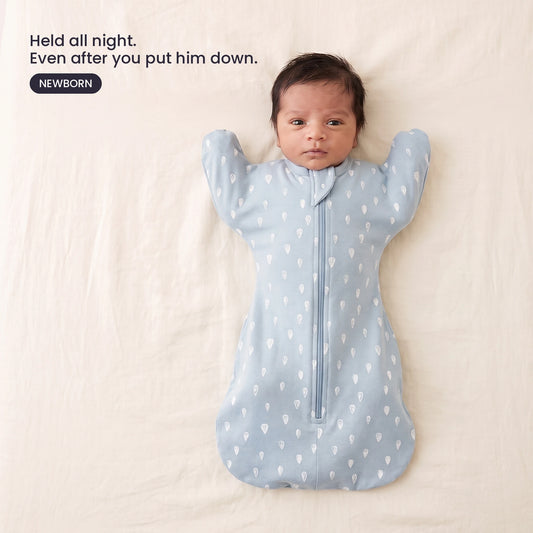 LIOR Held Swaddle Sack in Dusty Blue Drops - newborn asleep on their back in a crib, wearing the zip-up sack.