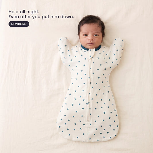 LIOR Held Swaddle Sack in Cream Ink Triangle - newborn asleep on their back in a crib, wearing the zip-up sack.