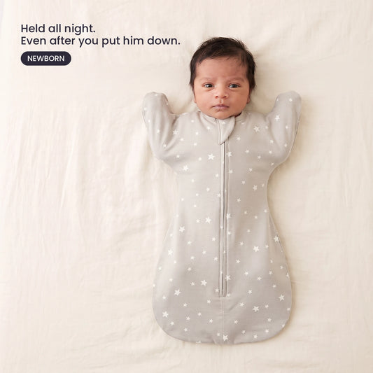 LIOR Held Swaddle Sack in Oat Stars - newborn asleep on their back in a crib, wearing the zip-up sack.